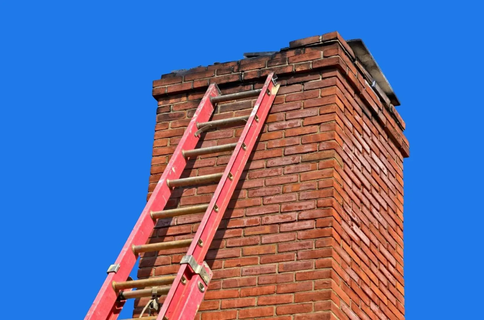 A ladder is attached to the side of a brick chimney.