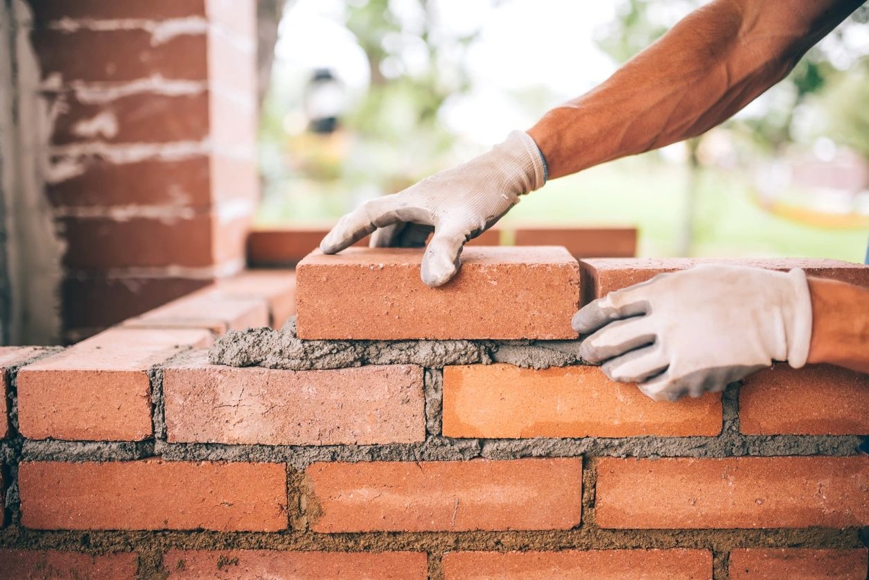 A person is building a brick wall with cement.